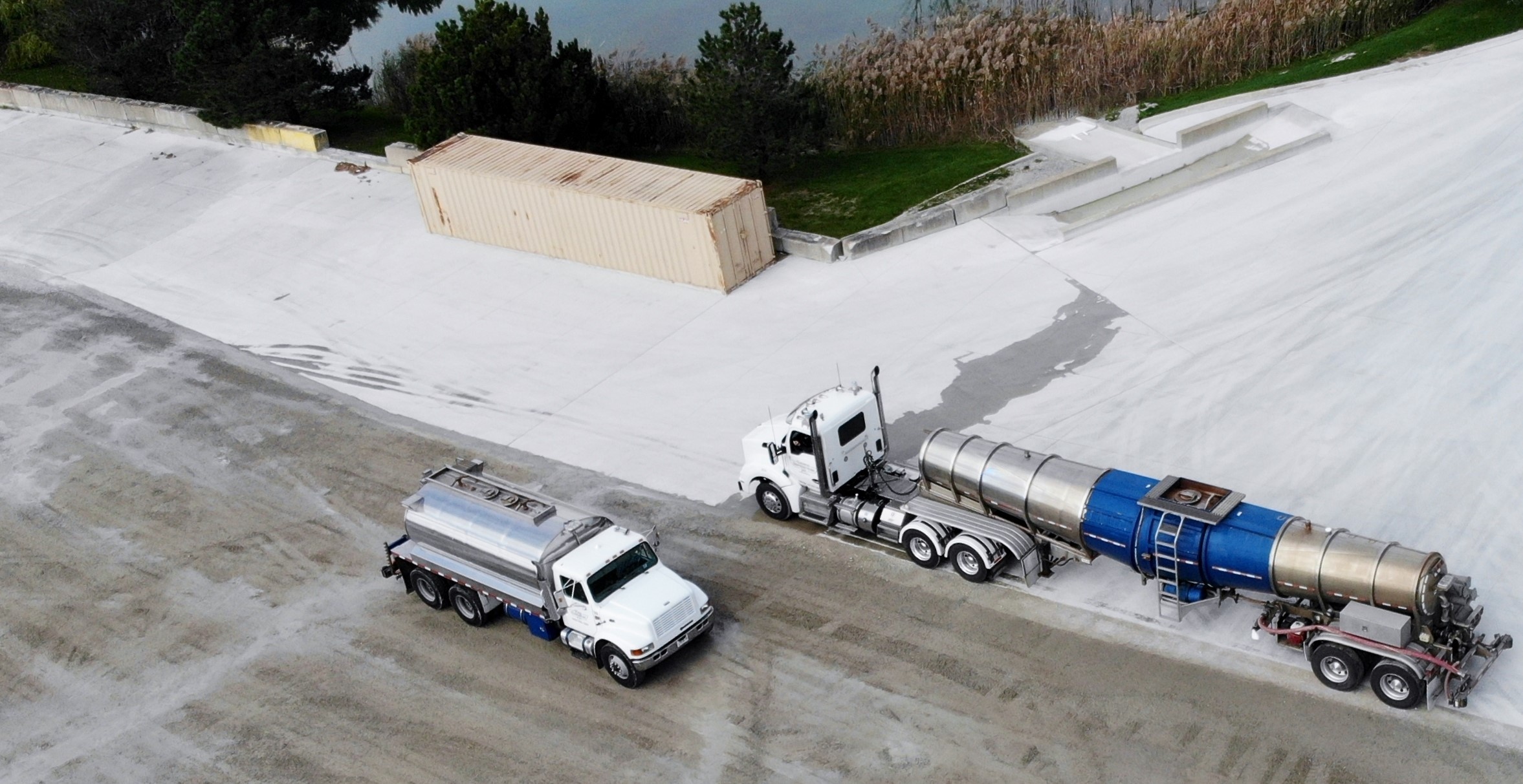 Two Gasaway Maintenance Company trucks, a 6,000-gallon tanker and a smaller tanker, applying dust control suppressants to a dusty lot.