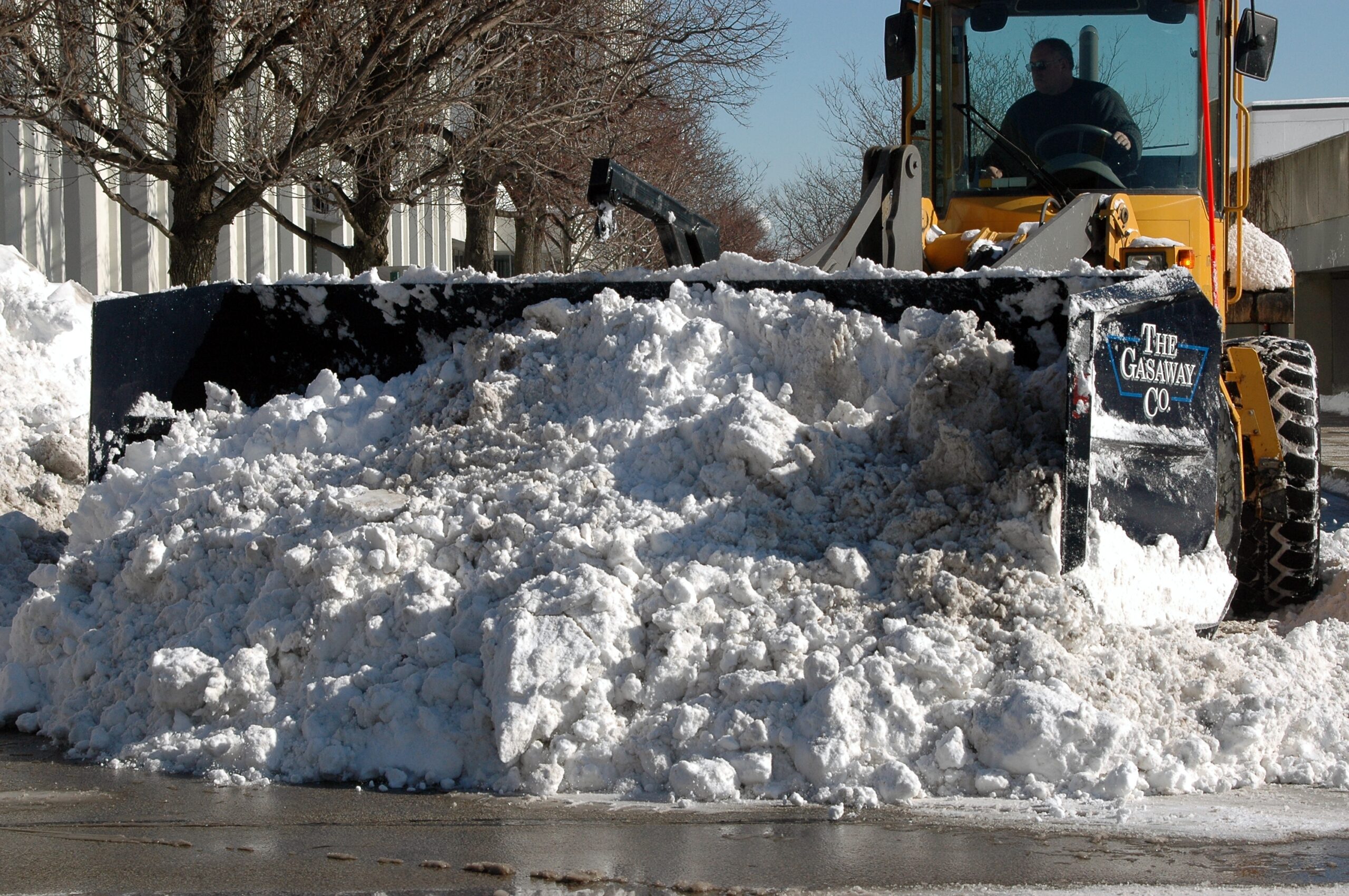 A massive pile of snow being plowed by a Gasaway Maintenance Company plow in a commercial parking lot.